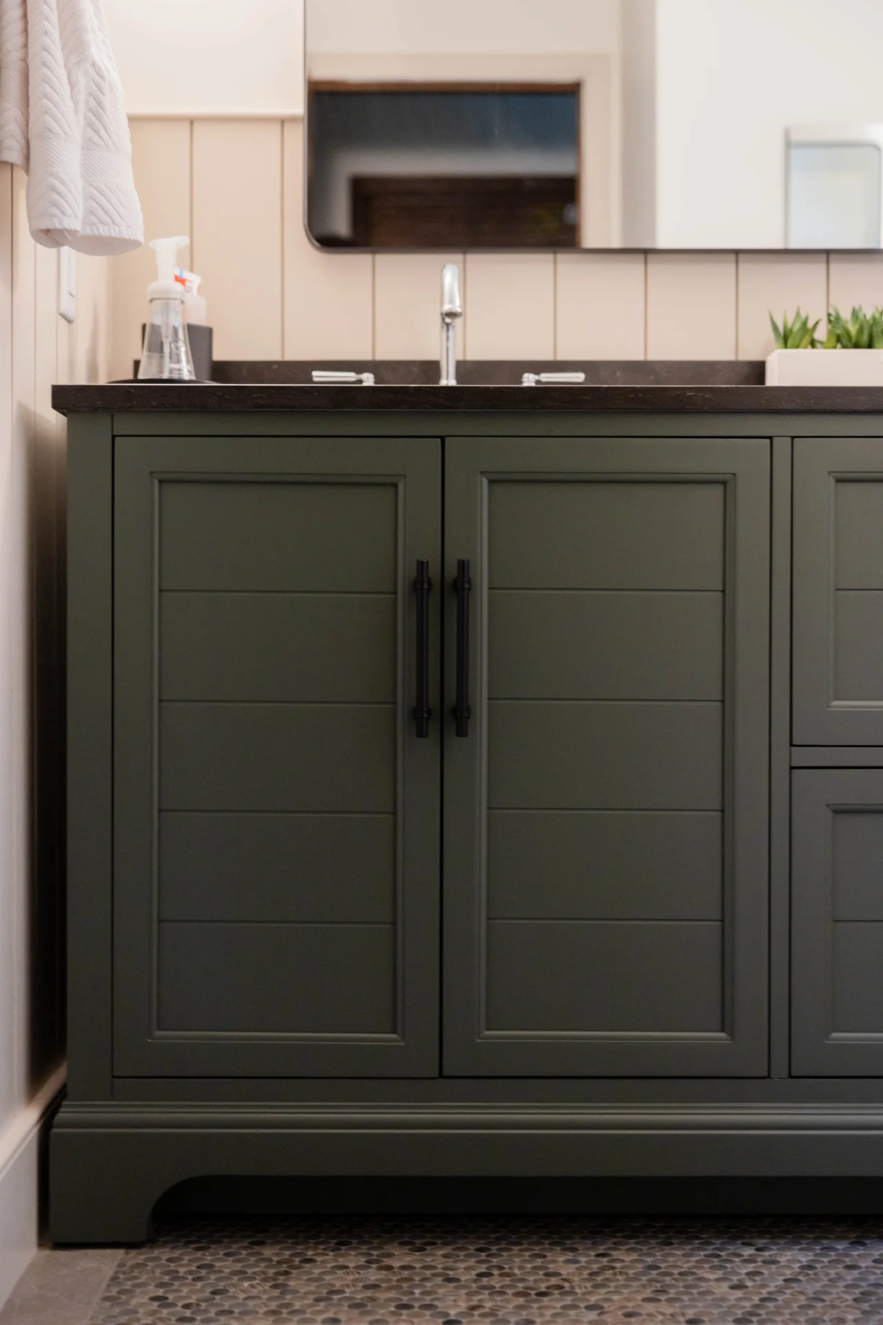 A green paneled vanity with a dark countertop and understated hardware.